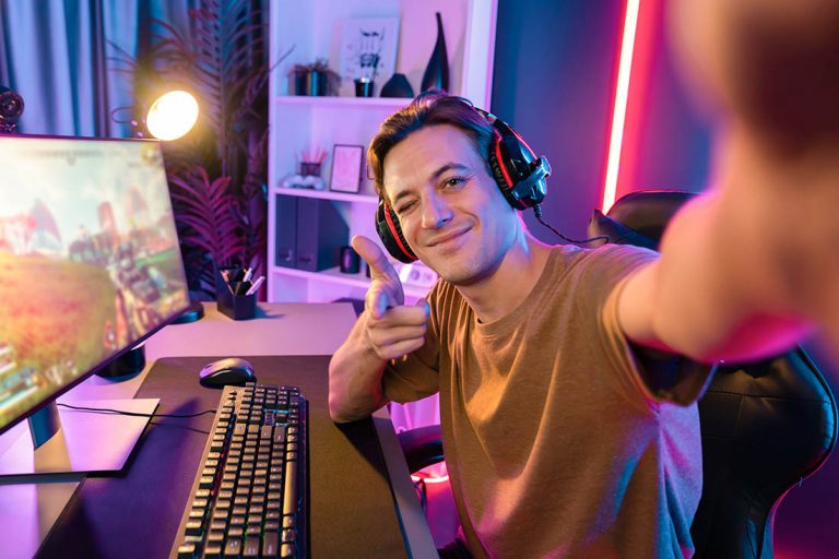 Host channel of smart gaming streamer looking at camera with playing battle team shooting gun background at warship on screen at back side view, wearing headset at digital neon cyber room. Pecuniary.